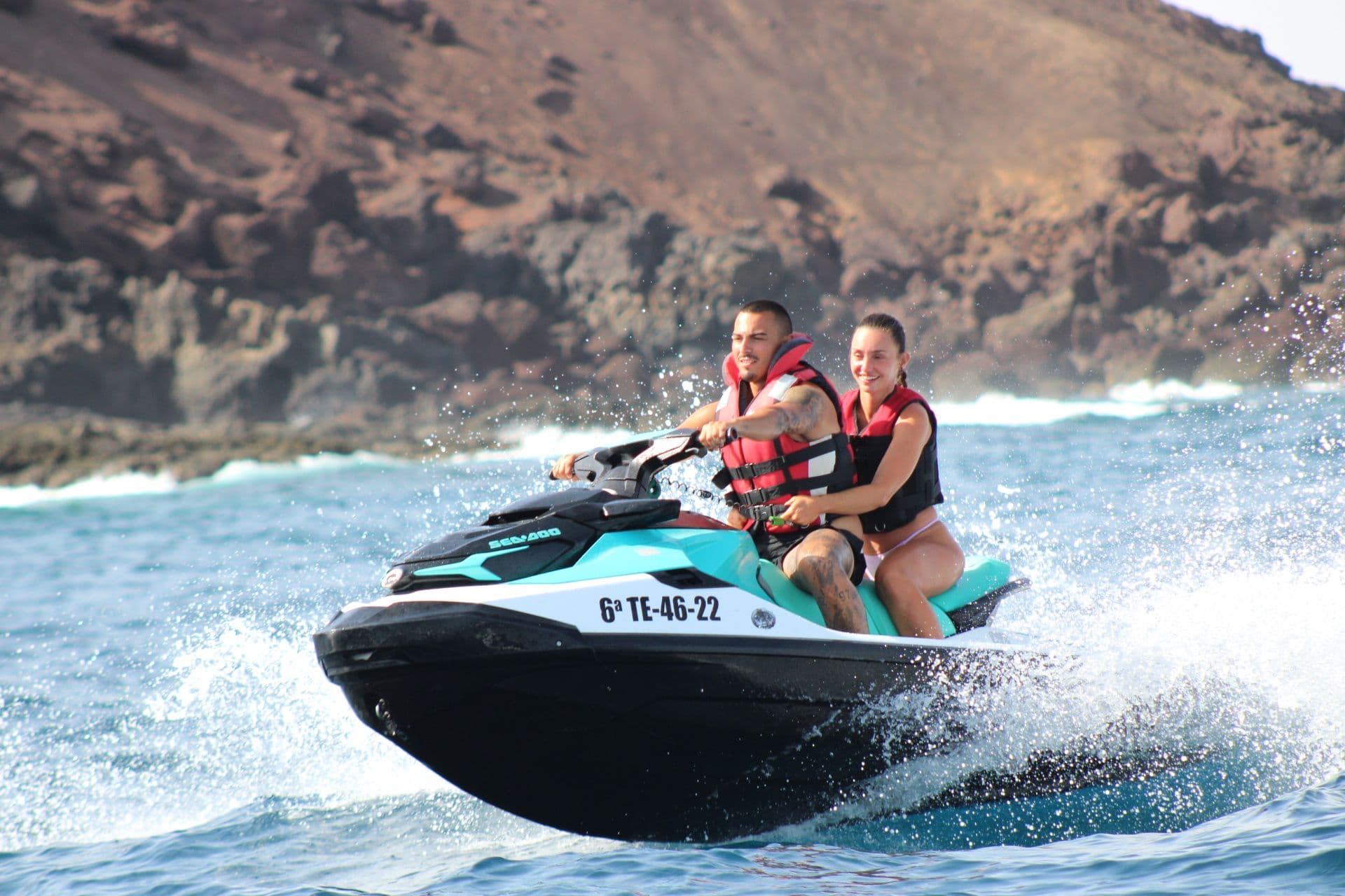 Couple on a turquoise jet ski passing the dark lava cliffs of Isla de Lobos