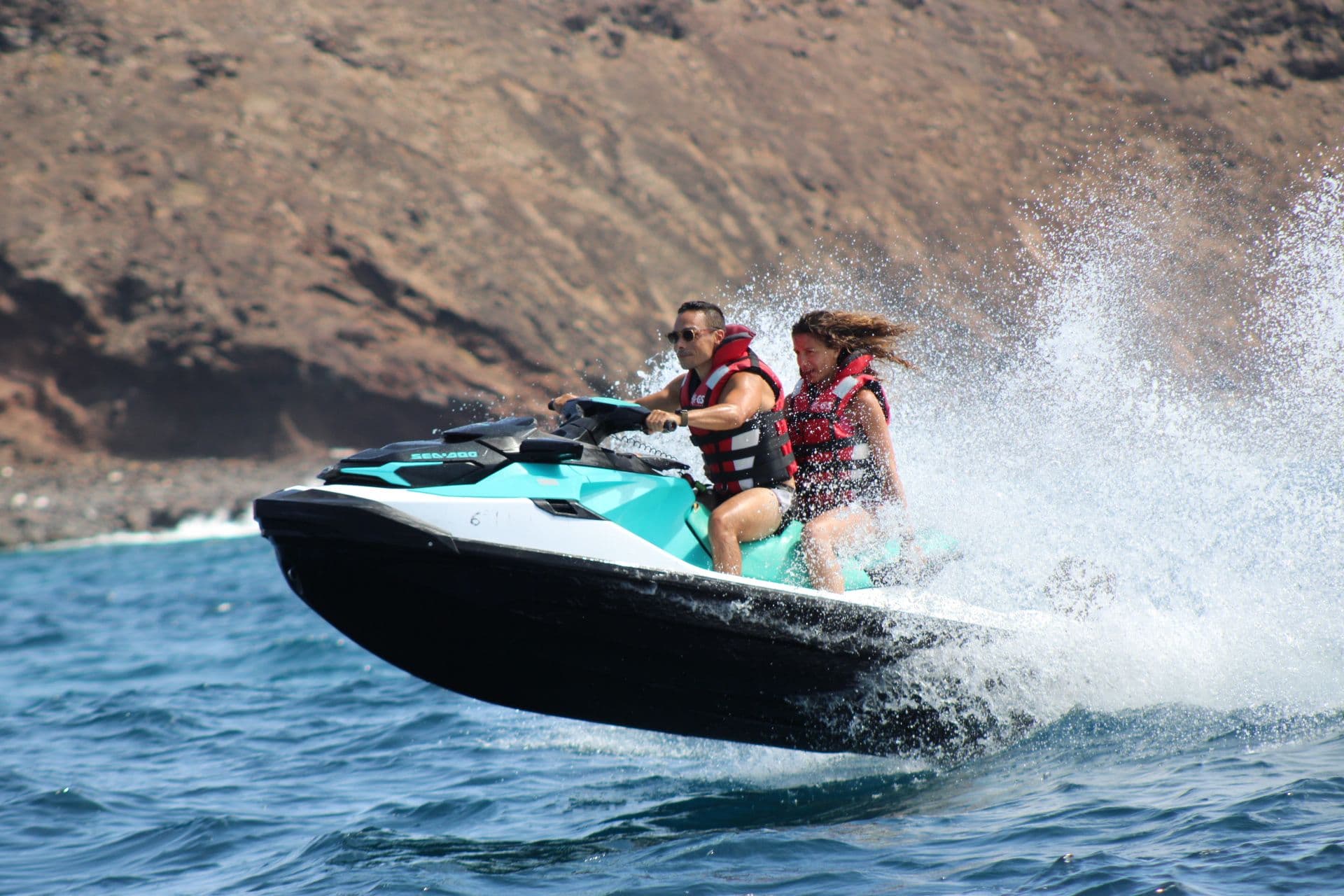 Couple on a turquoise Sea-Doo with spray flying in front of a lava cliff on Isla de Lobos