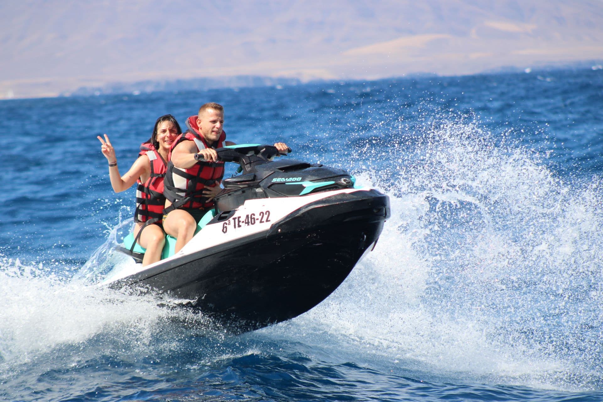 Couple on a turquoise jet ski, the passenger making a peace sign, on the waves off Fuerteventura