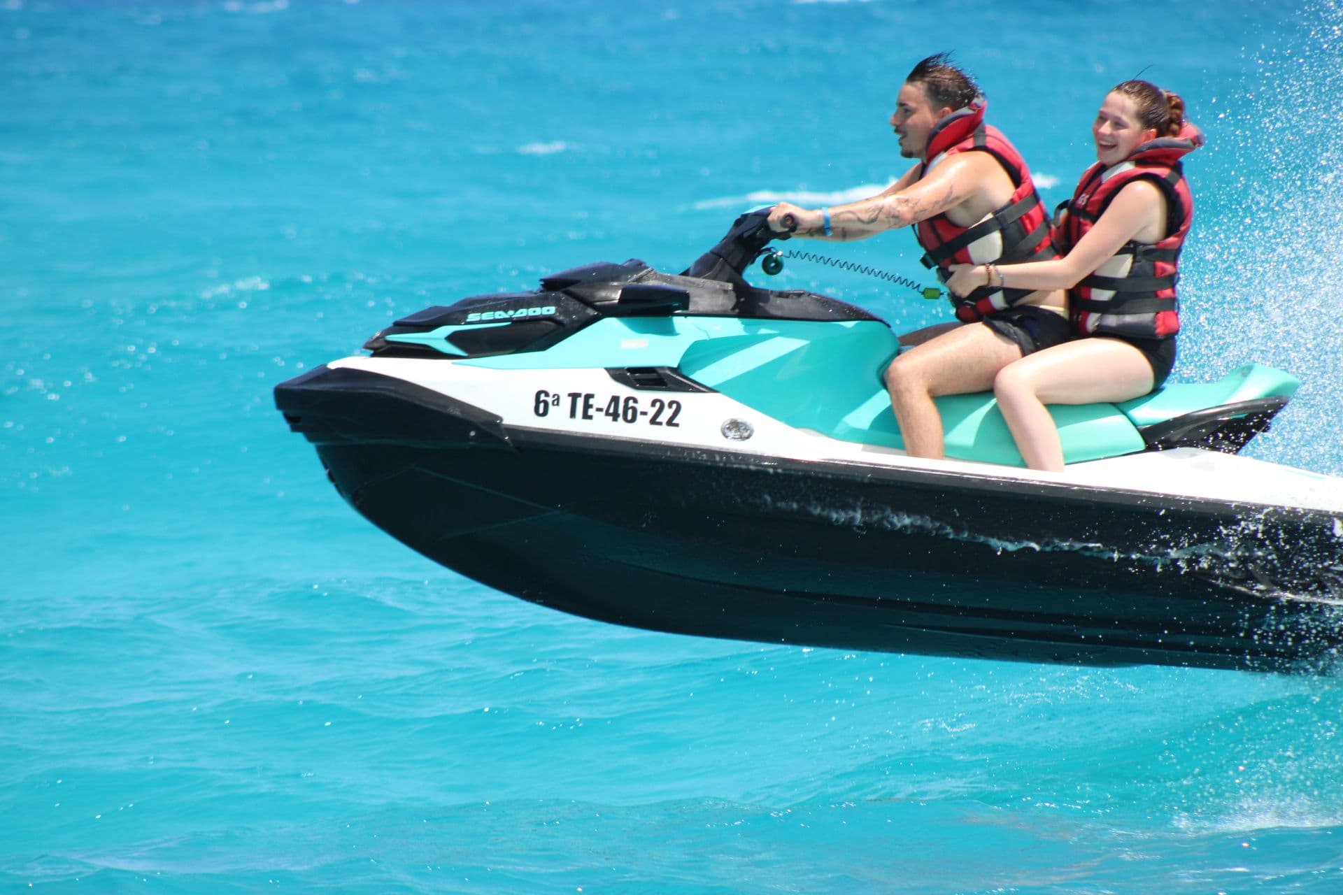 Two riders on a turquoise and white Sea-Doo jet ski skimming over bright turquoise water near Corralejo