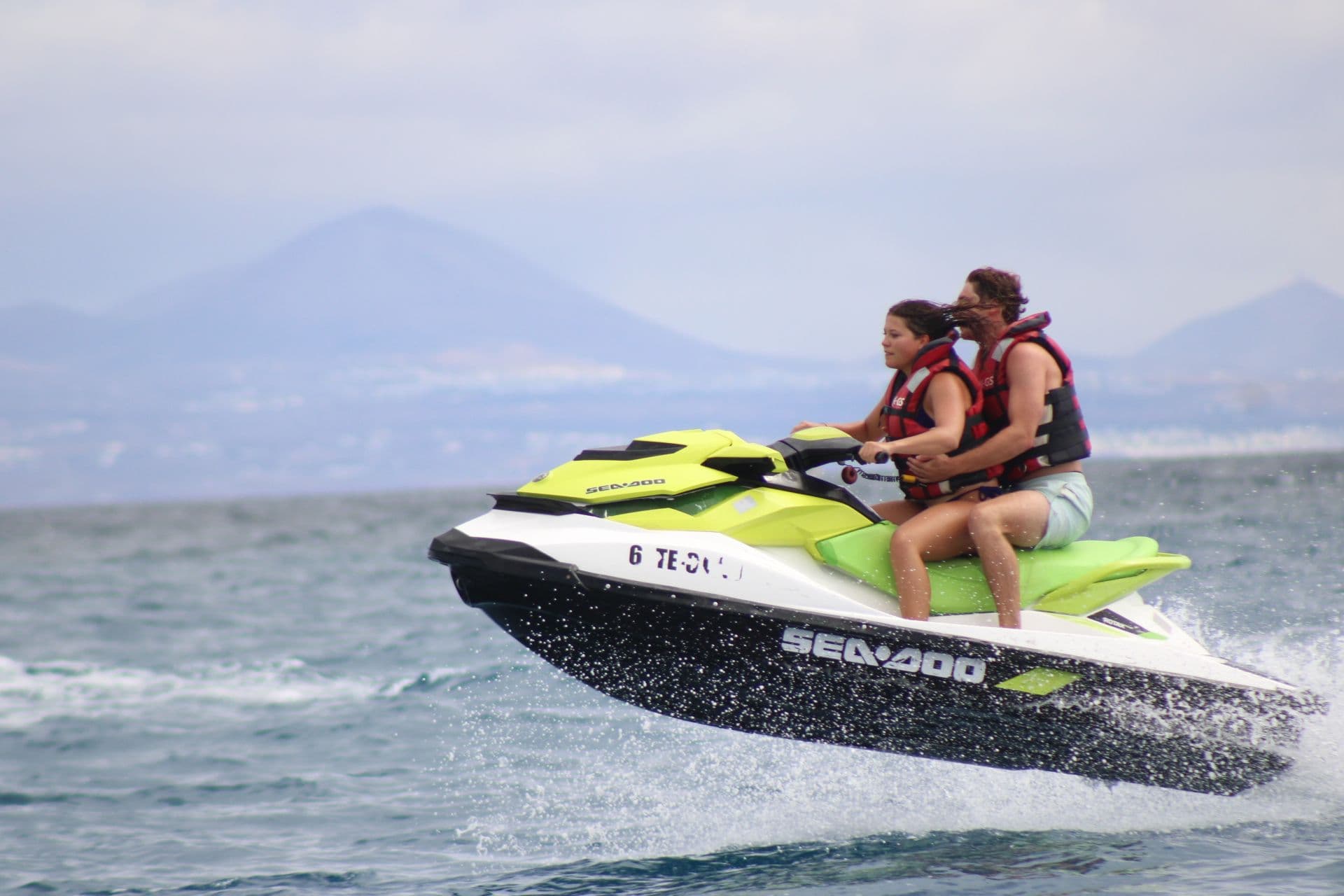 Couple airborne on a lime and white Sea-Doo with the mountains of Lanzarote behind
