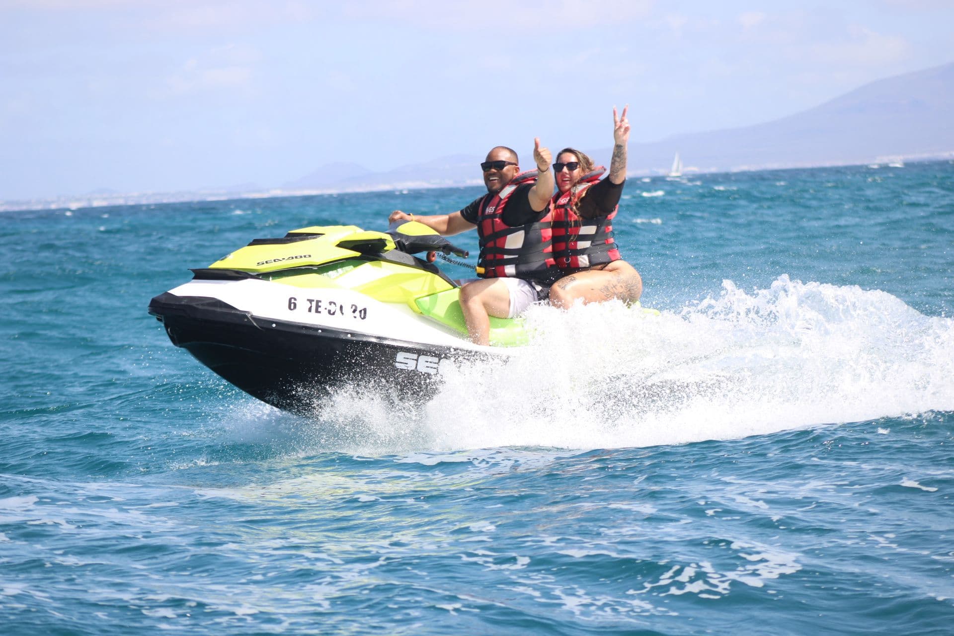 Couple waving from a lime and white Sea-Doo jet ski on the Atlantic off Corralejo