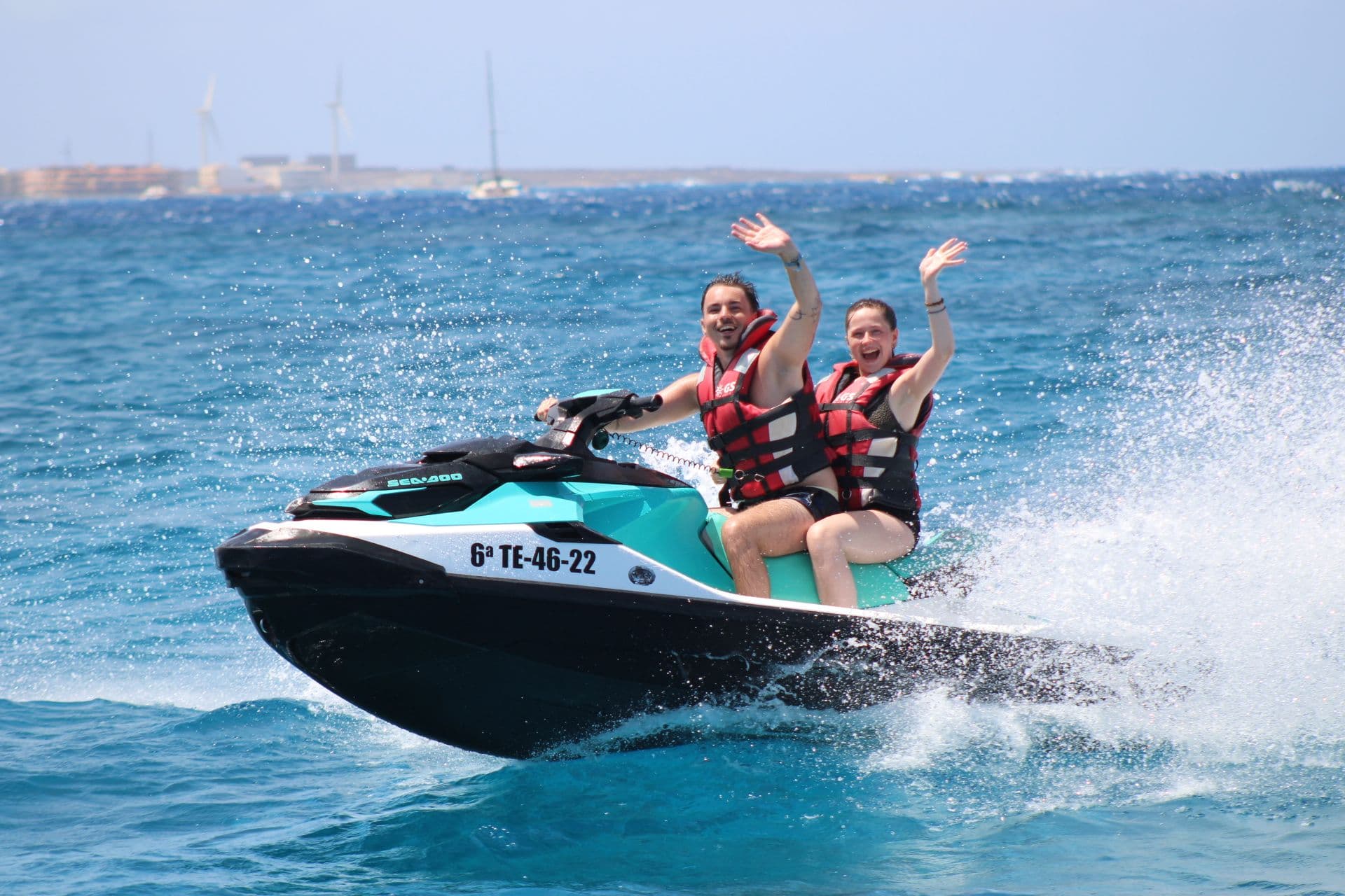 Two friends waving from a turquoise Sea-Doo jet ski on the open Atlantic off Fuerteventura