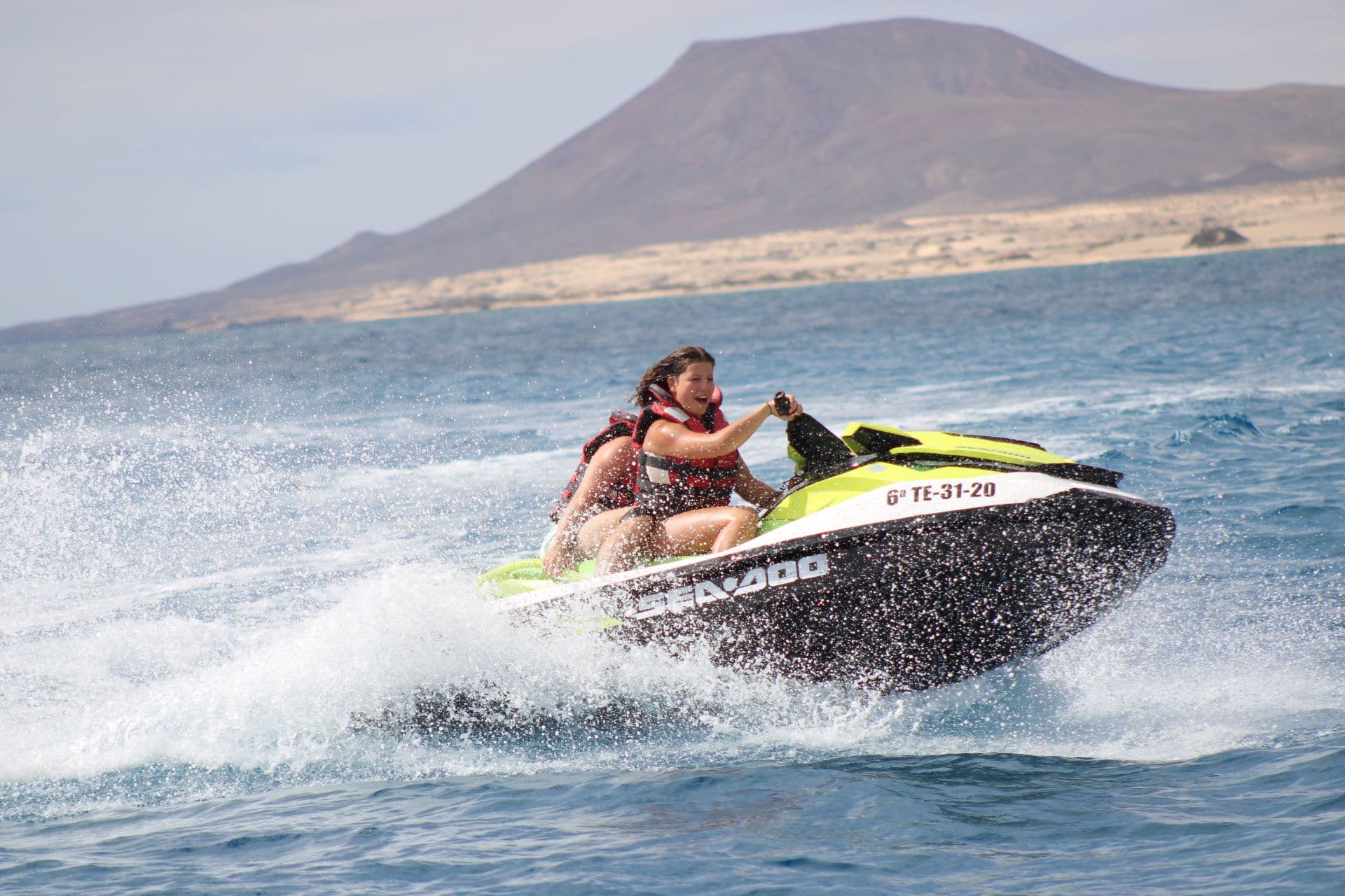 Two riders on a lime Sea-Doo in front of a volcanic mountain above the Corralejo dunes