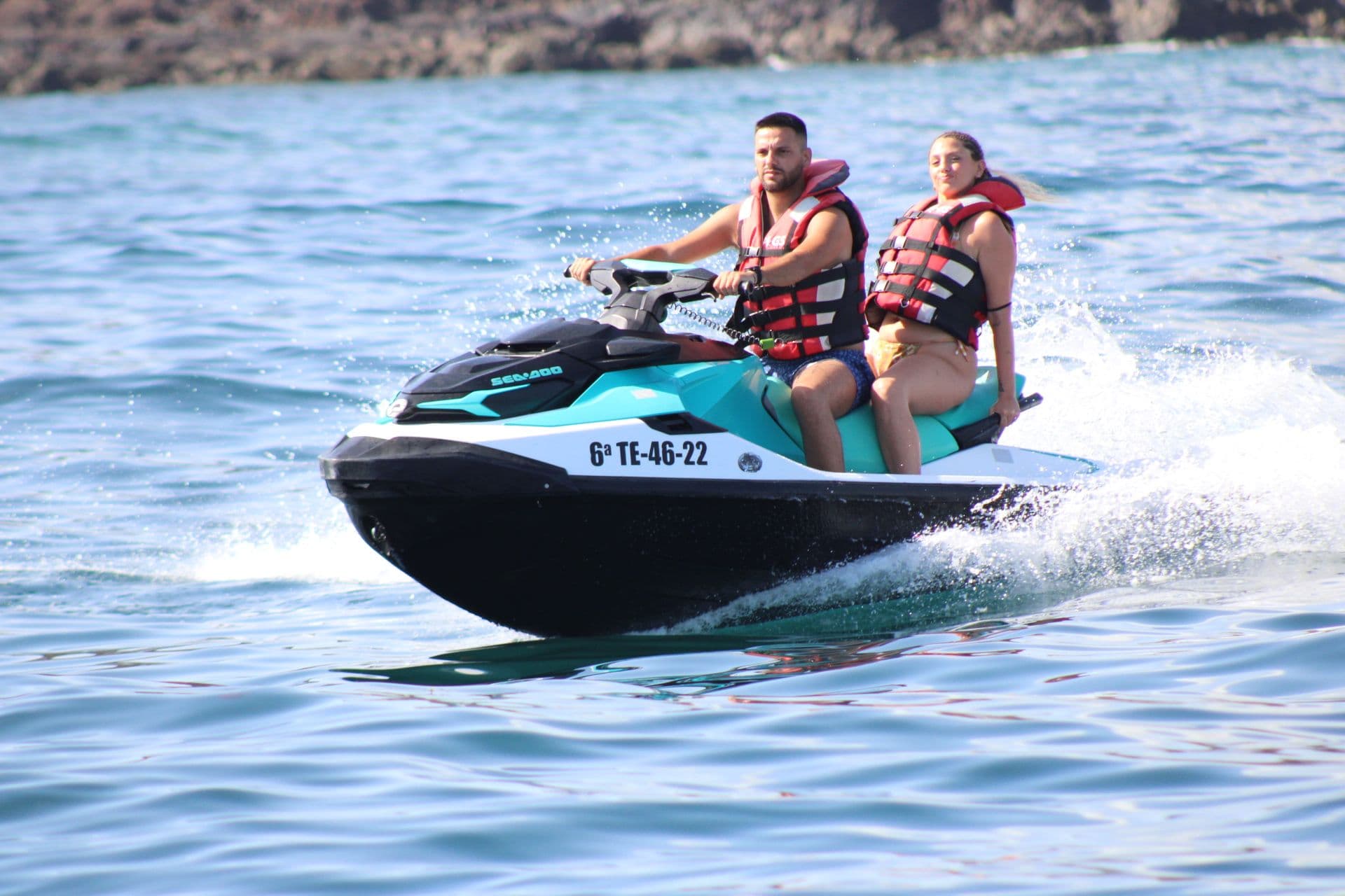 Smiling couple in red life vests riding a turquoise and white Sea-Doo jet ski off Corralejo