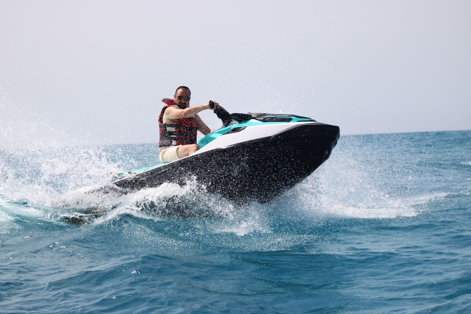 Solo rider leaning into a turn on a turquoise jet ski with spray across the Atlantic
