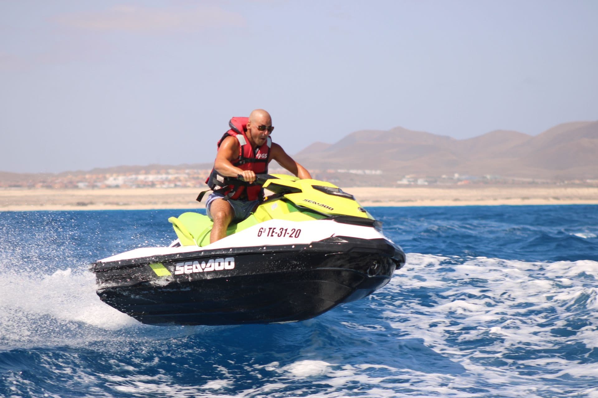 Solo rider on a lime and white Sea-Doo jet ski with the Corralejo dunes and mountains behind