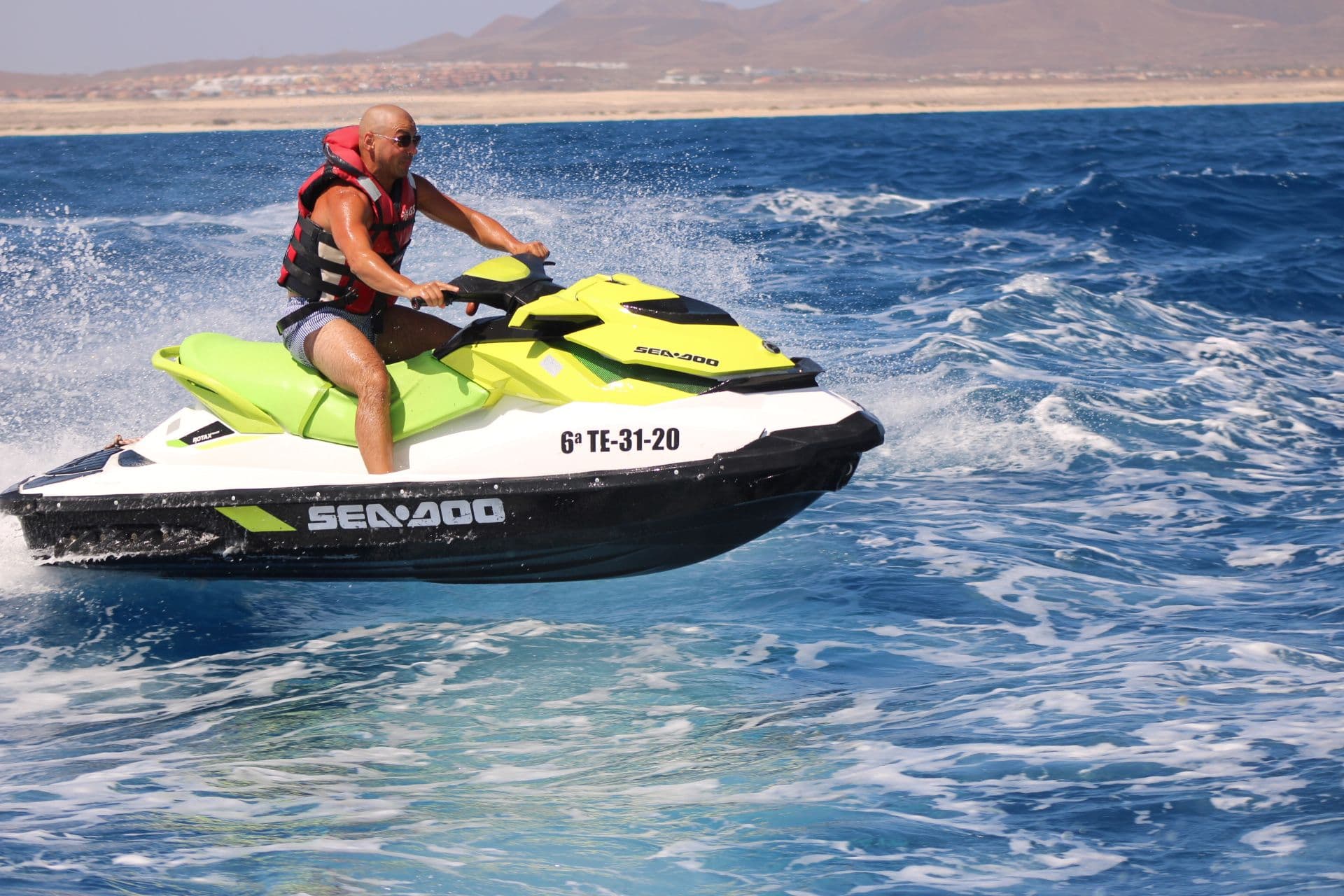 Solo rider carving through wake on a lime and white Sea-Doo jet ski off Corralejo