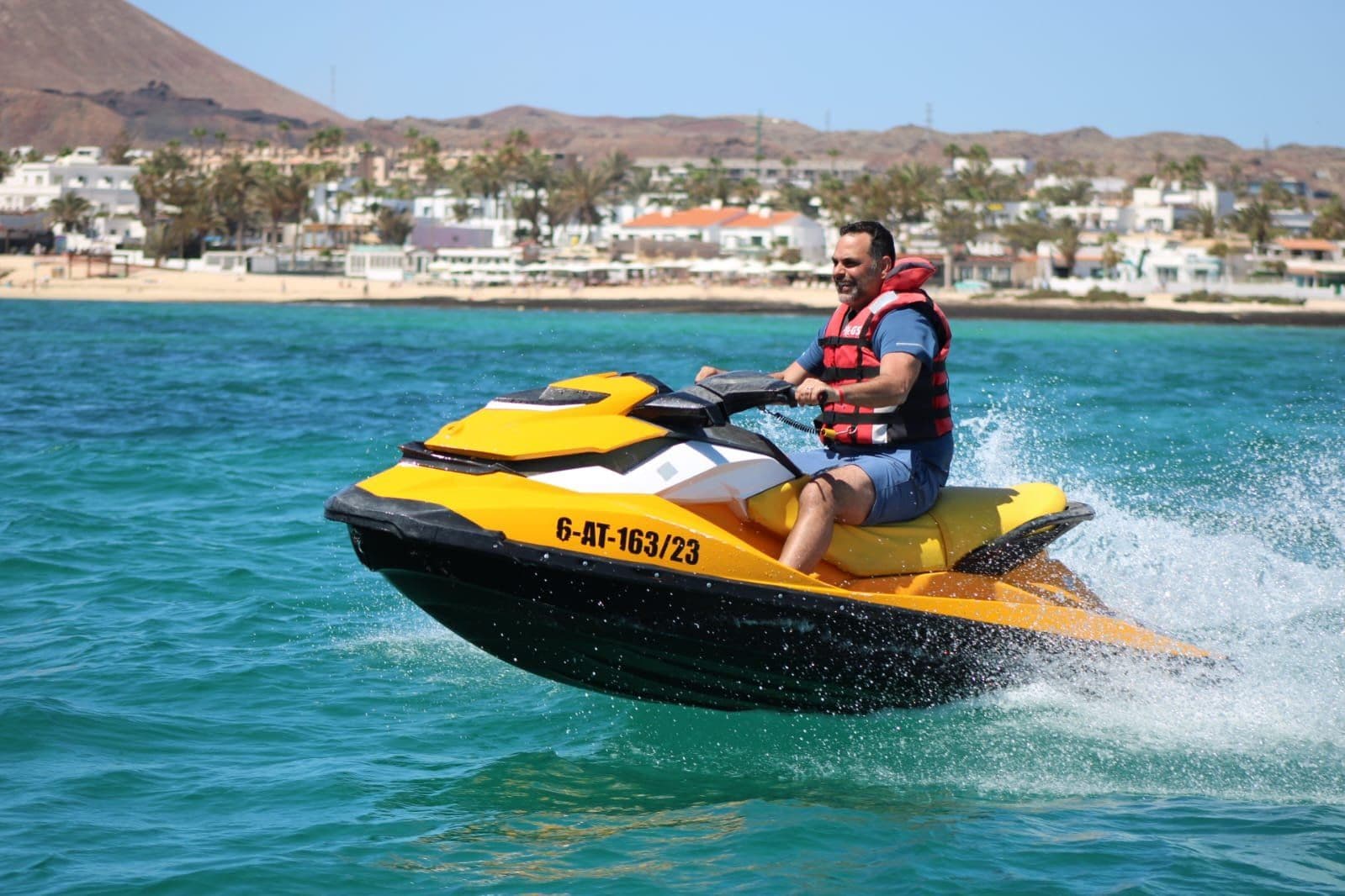 Couple in red life vests catching air on a yellow Sea-Doo jet ski with sunglasses and big smiles