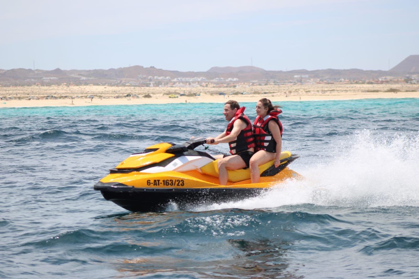 Solo male rider in red shorts and life vest catching air on a yellow Sea-Doo jet ski over the deep blue Atlantic