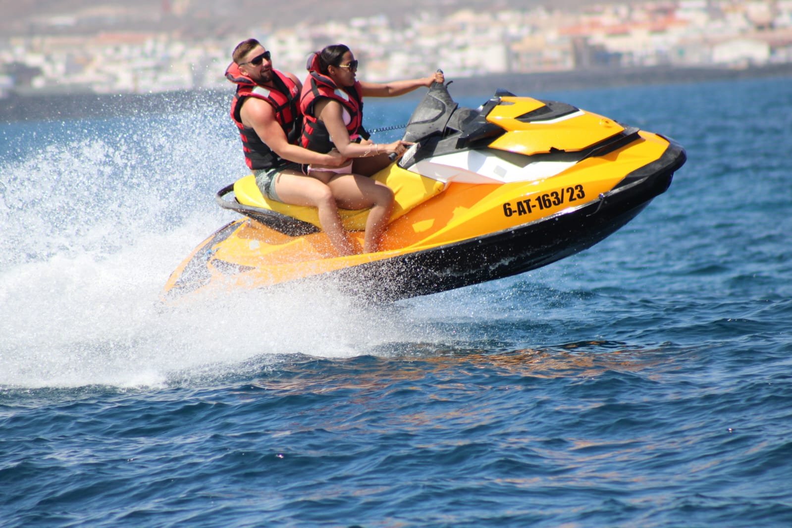 Couple wearing sunglasses and red life vests cruising calm turquoise water on a yellow Sea-Doo jet ski