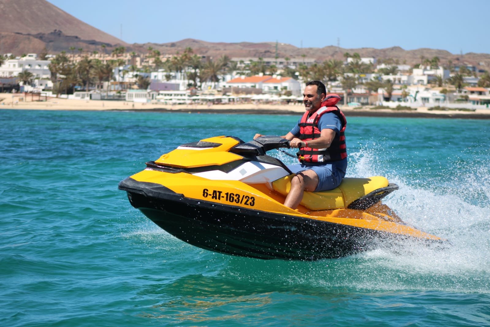 Couple in red life vests catching air on a yellow Sea-Doo jet ski with sunglasses and big smiles