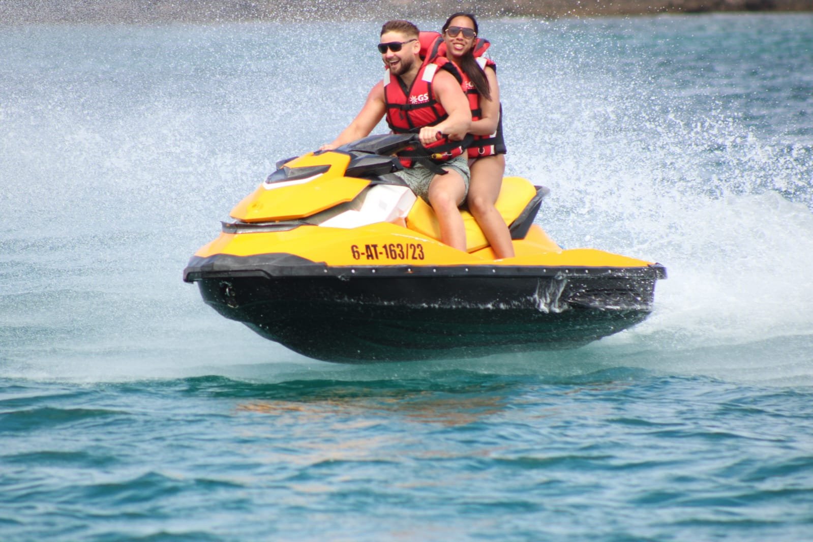 Couple riding a yellow Sea-Doo jet ski with bright white spray on the calm Atlantic off Corralejo