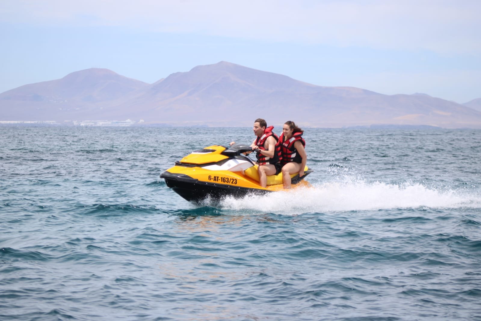 Couple riding a Sea-Doo jet ski with the Montaña La Caldera volcano of Isla de Lobos in the background