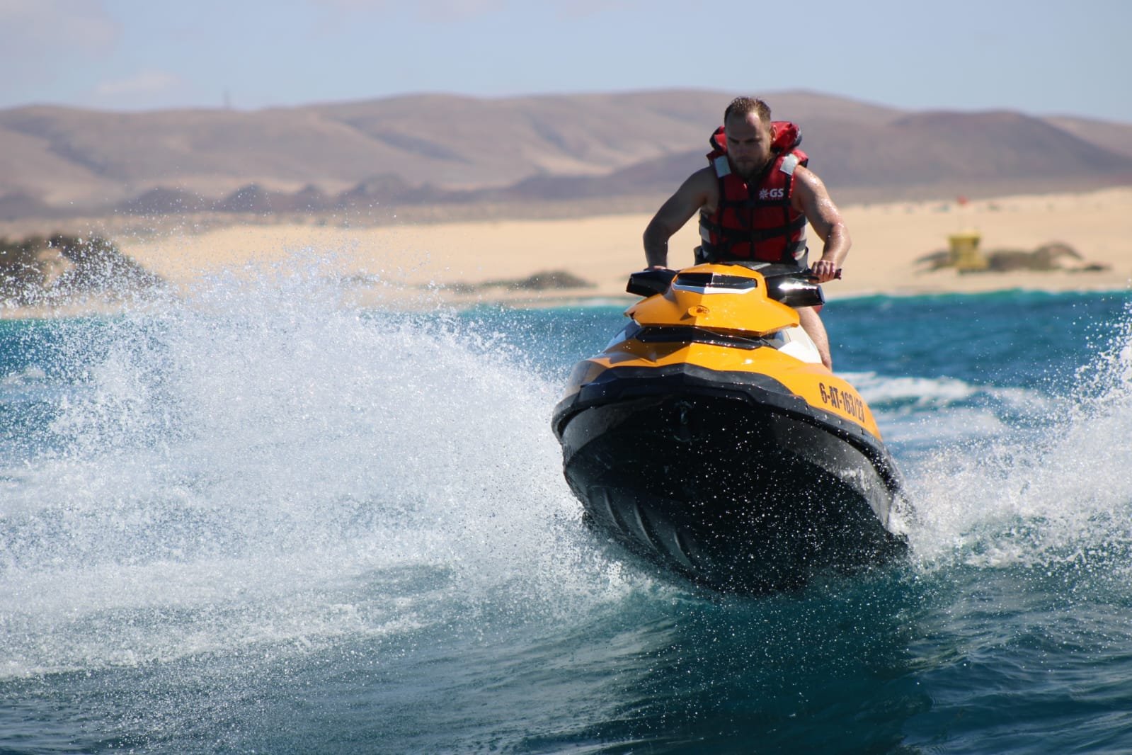 Couple smiling on a yellow Sea-Doo jet ski with the residential coast of Corralejo behind