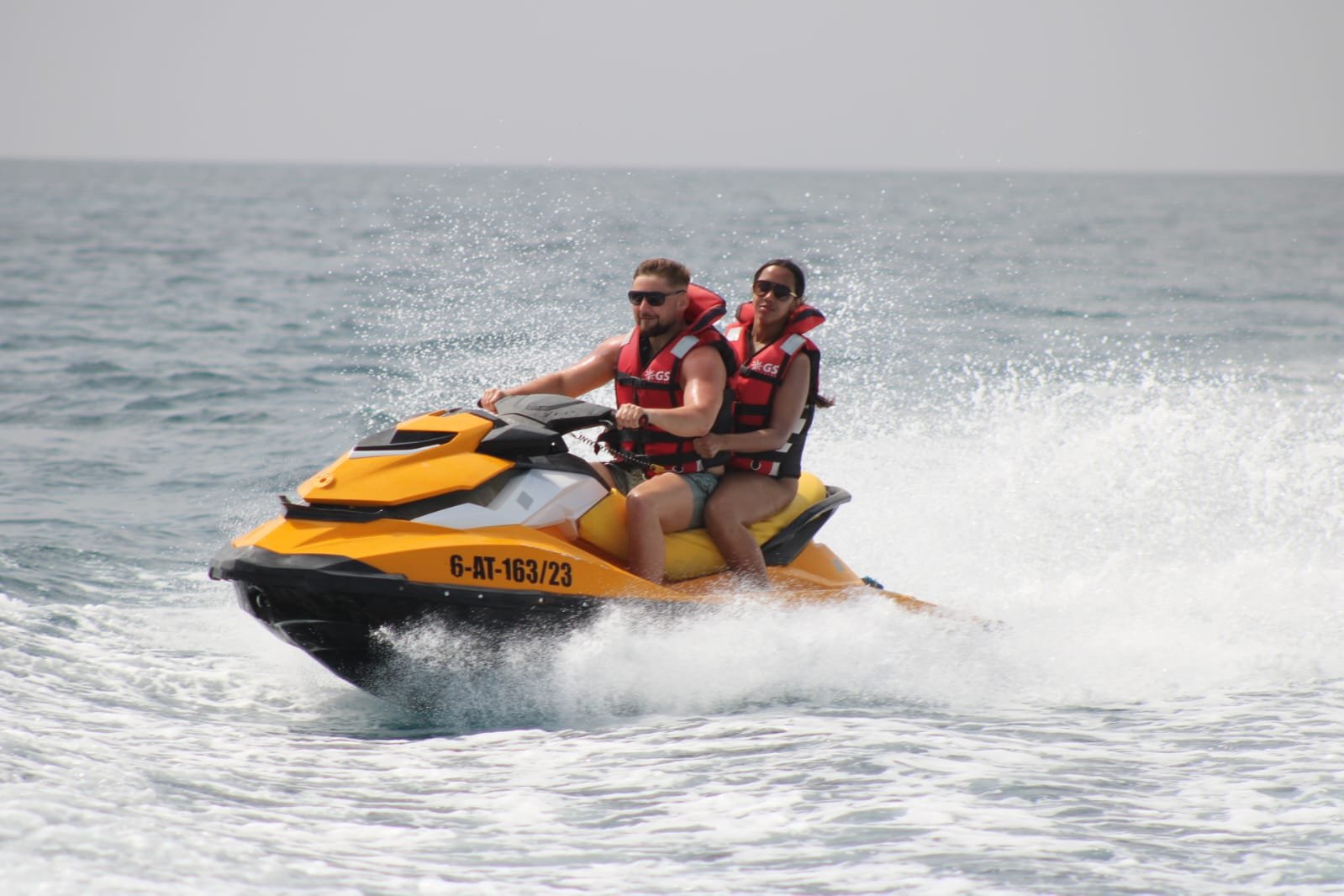 Smiling couple on a yellow Sea-Doo jet ski racing across the turquoise water of Corralejo bay