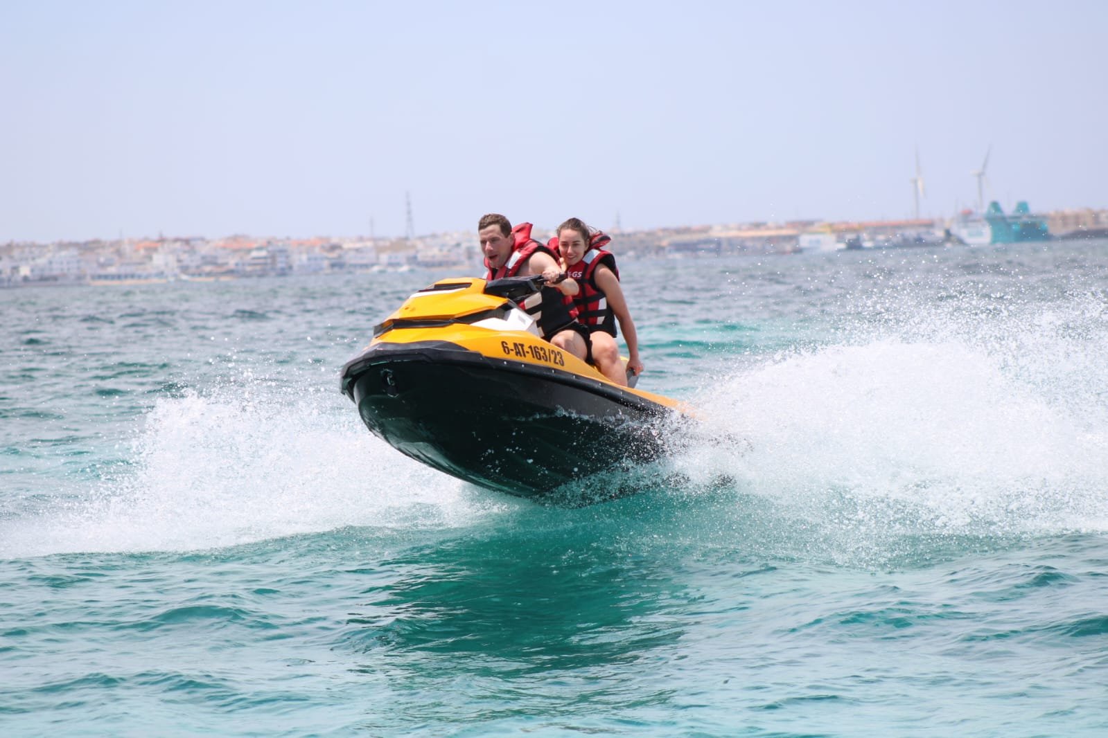 Yellow jet ski crashing through Atlantic waves with Corralejo coastline and beach hotels in the background