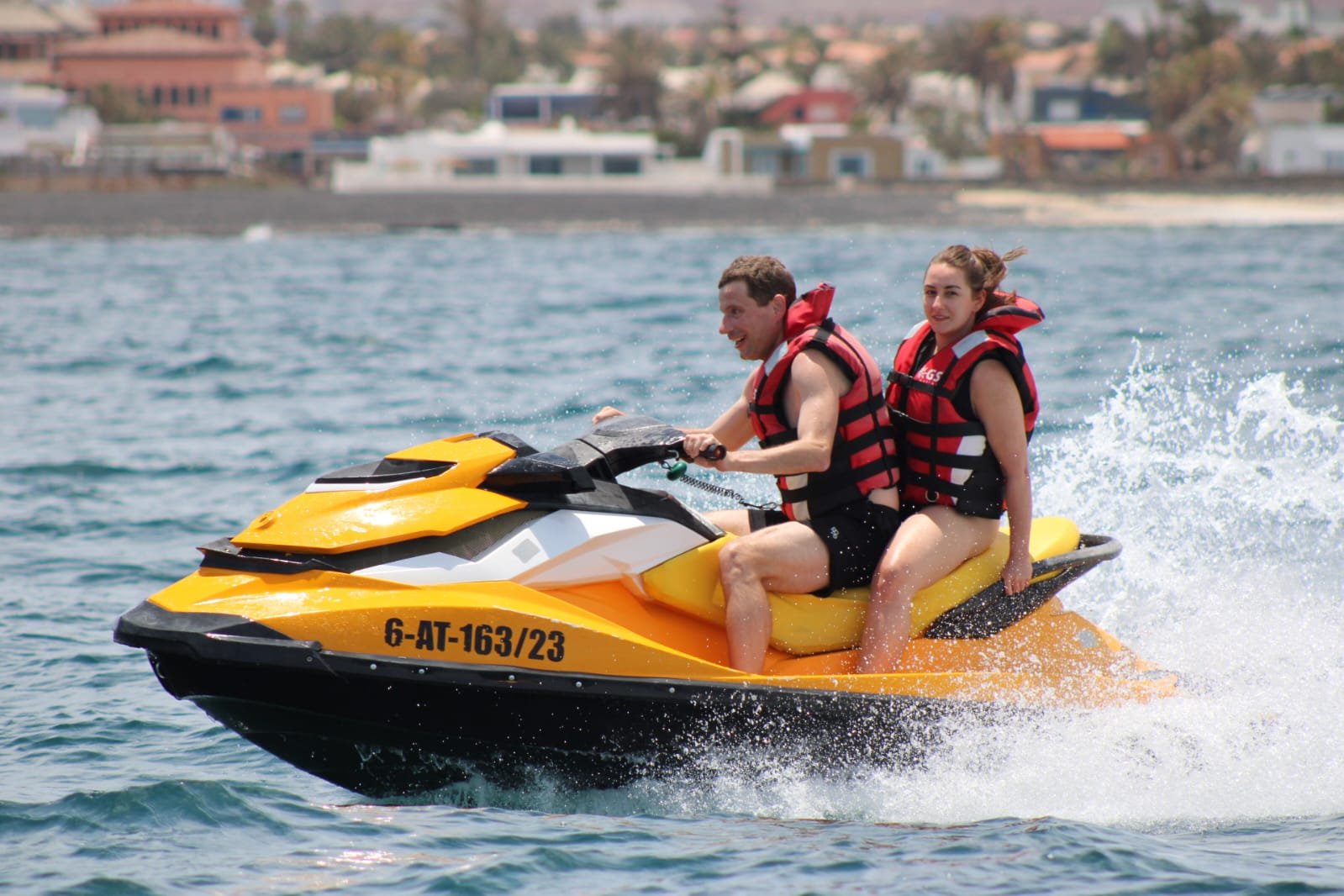 Solo male rider on a yellow jet ski jumping high above the deep blue water off Corralejo