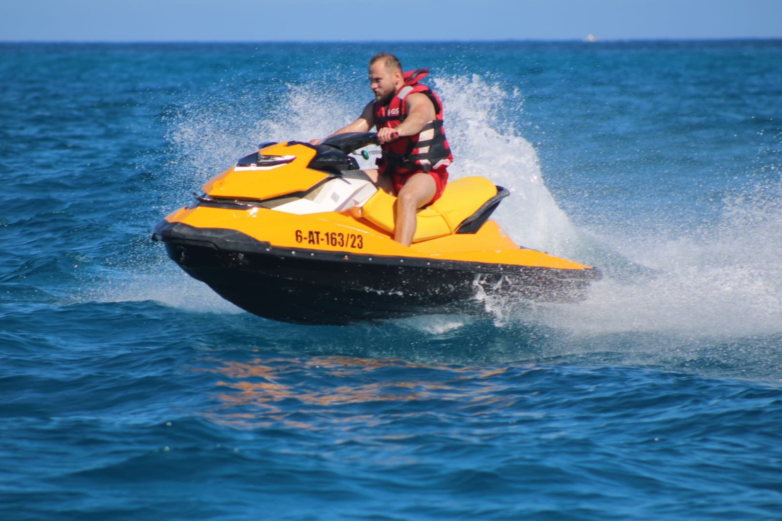 Solo rider on a yellow jet ski crossing the strait between Fuerteventura and Isla de Lobos with the volcanic island in the distance