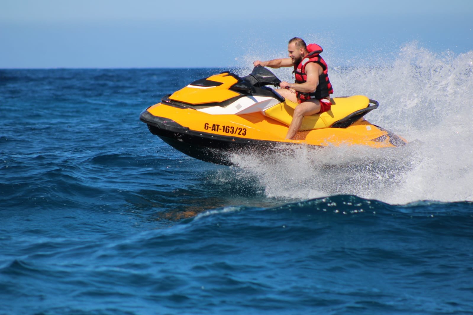 Front view of solo rider on a yellow jet ski with the iconic Corralejo sand dunes stretching behind