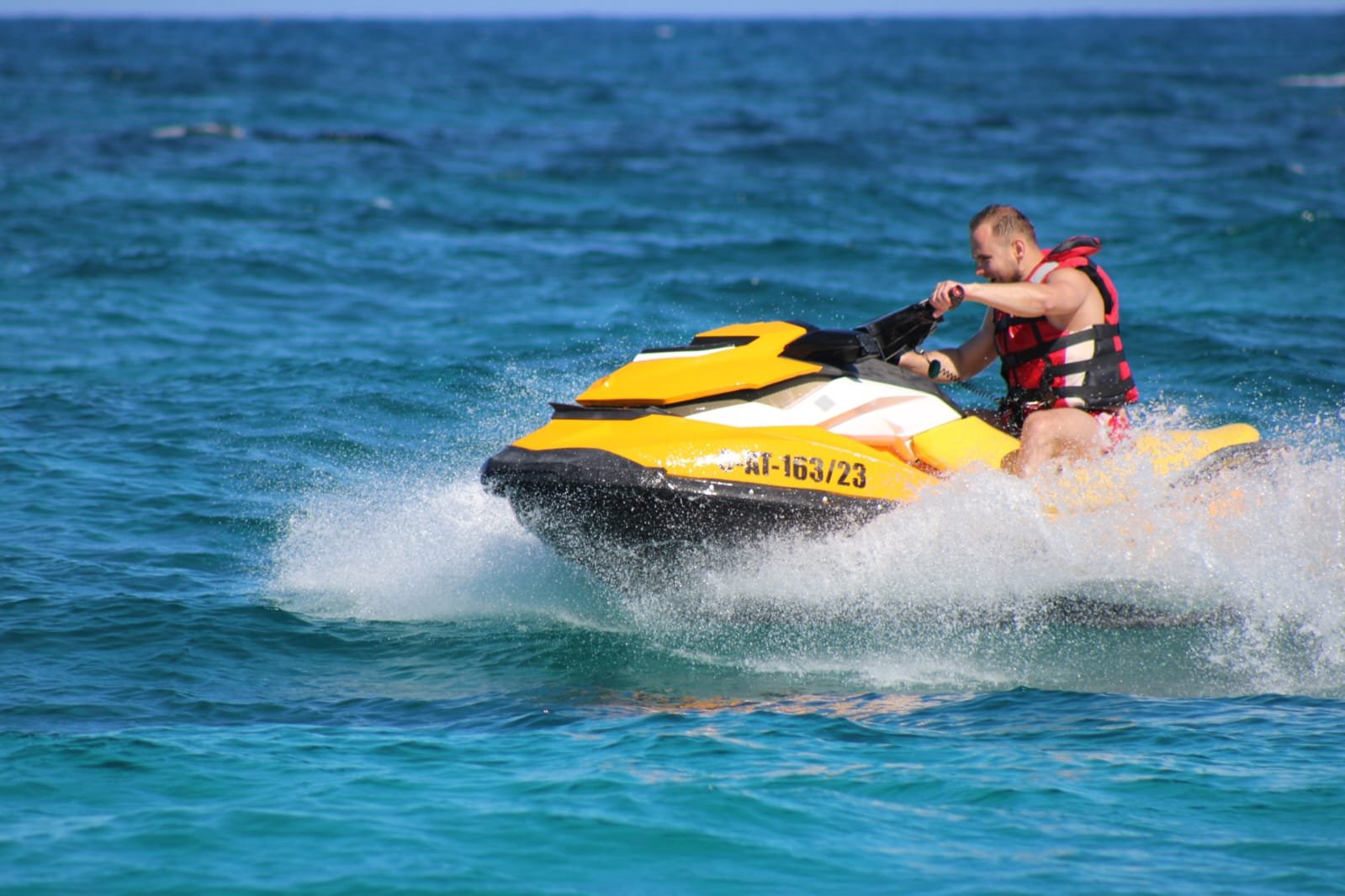 Solo male rider on a yellow Sea-Doo jet ski jumping a wave with white spray on the deep blue Atlantic
