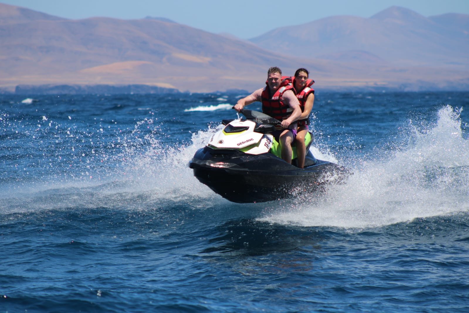 Solo rider on a yellow jet ski with the historic Punta Martiño lighthouse on Isla de Lobos directly behind