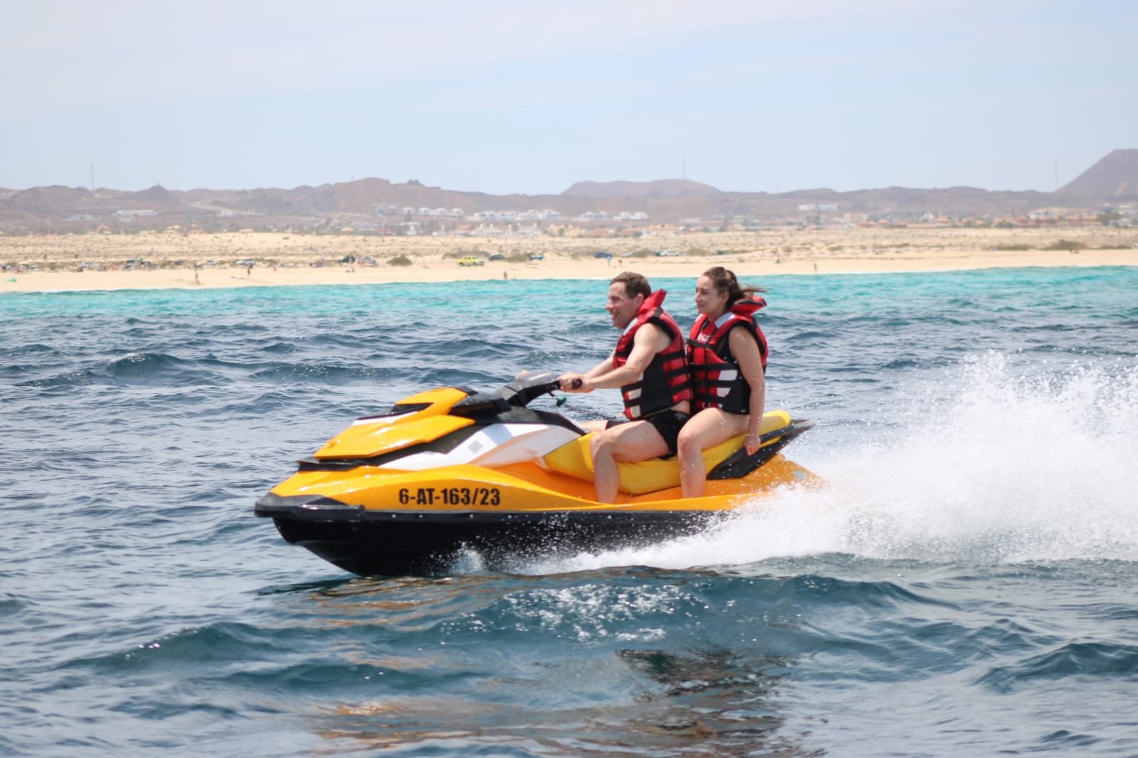 Solo male rider in red shorts and life vest catching air on a yellow Sea-Doo jet ski over the deep blue Atlantic