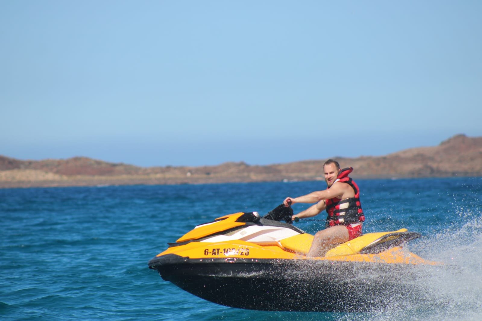 Solo rider in red shorts riding a yellow Sea-Doo jet ski across calm turquoise water near Corralejo
