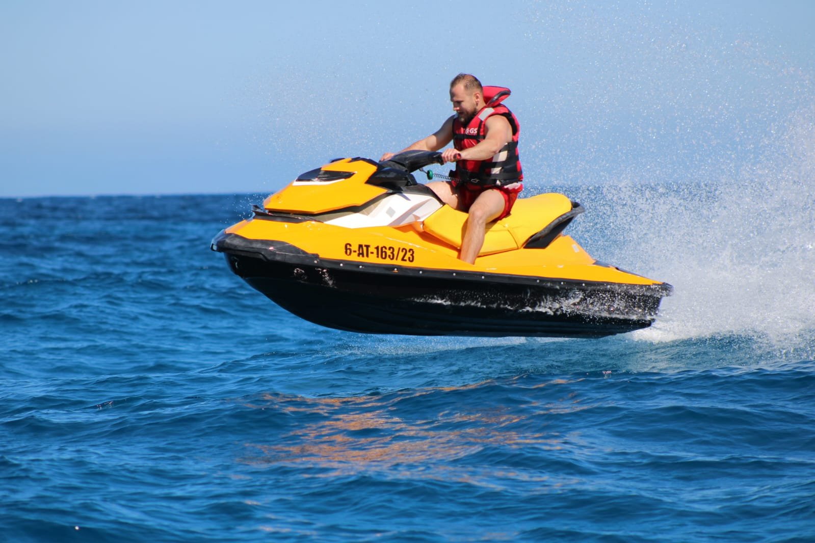 Solo rider on a yellow jet ski with the volcanic landscape of Isla de Lobos behind, mid-tour